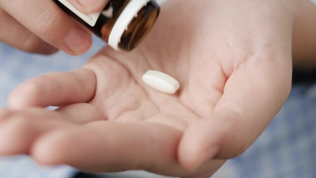 Two big white pills oval diamond-shaped elongated shapes fall into palm of hand from pill bottle. Close-up, front view, center composition