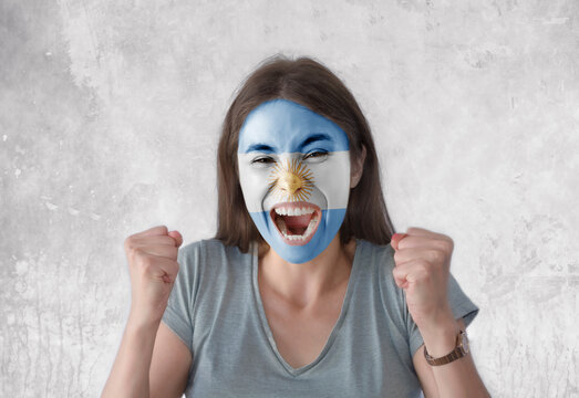 Young woman with painted flag of Argentina and open mouth looking energetic with fists up