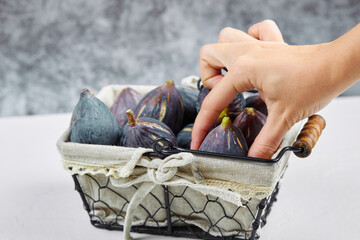Hand holding a fig from the basket on a white and marble background