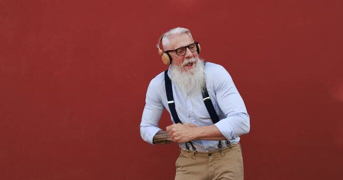Happy senior man dancing and listening music outdoor with headphones - Joyful elderly lifestyle and technology concept