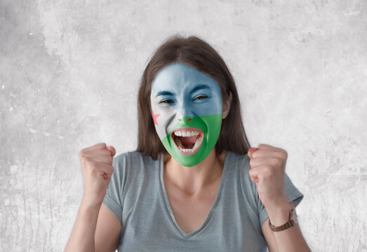 Young woman with painted flag of Djibouti and open mouth looking energetic with fists up