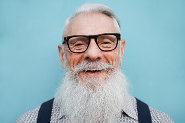 Portrait of hipster senior bearded man wearing glasses with blue desaturaded background