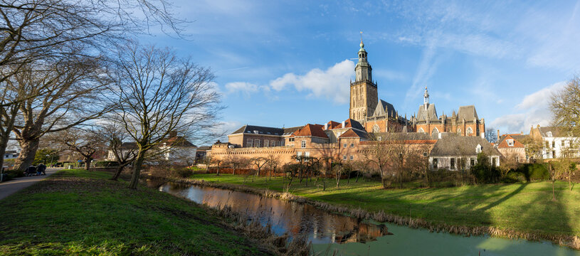 Picturesque wide panoramic view of medieval Hanseatic city Zutphen in The Netherlands against a blue sky with clouds lit up by afternoon sun with lush winter garden in the foreground