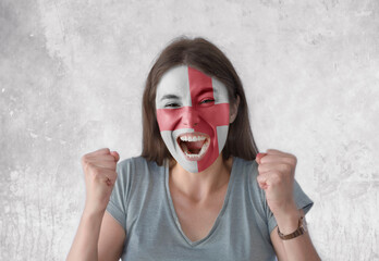 Young woman with painted flag of England and open mouth looking energetic with fists up
