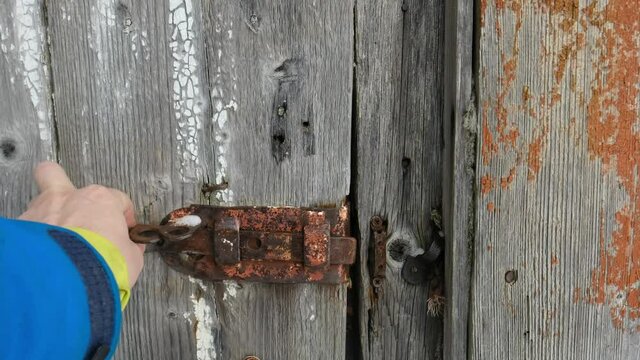 man's hand opens a wooden door. old rusty lock, bolt