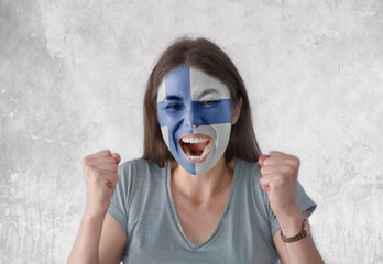 Young woman with painted flag of Finland and open mouth looking energetic with fists up