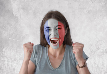 Young woman with painted flag of France and open mouth looking energetic with fists up