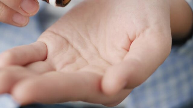 Two big white-yellow cylindrical capsule pills fall into palm of hand from pill bottle. Close-up, front view, center composition
