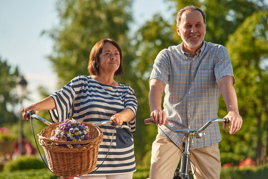 Elder man and woman outoodrs in the park. Aged caucasian couple with bikes and flowers.