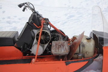 Old Soviet utility snowmobile without hood close up - steering, air cooled engine with emergency start handle and fuel tank
