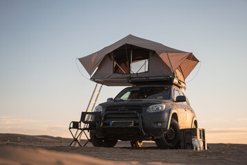 Rooftop tent for camping on the roof rack of an off-road SUV car in a desert