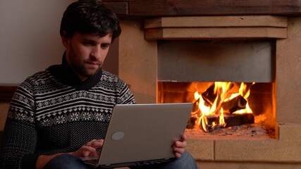 Woman using a digital laptop sits by the fireplace