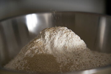 Human hands add salt and yeast to wholemeal flour dough to make bread, pasta, cake or pizza. The cook on the wooden table of his kitchen carries on the tradition of homemade pasta.