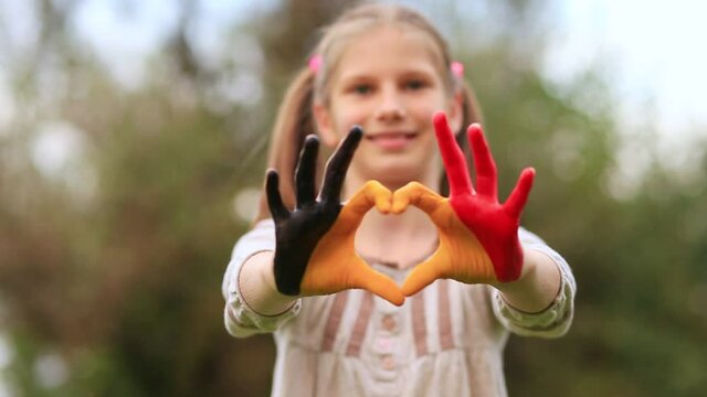 Kid hands painted in Belgium flag color show symbol of heart and love gesture on nature background. Focus on hands