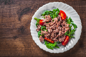 Tuna salad with arugula and tomatoes in white plate on wooden table background