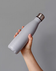 Hand with grey rinsulated bottle on grey background