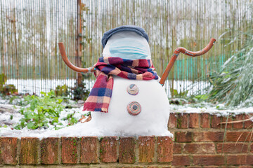 A snowman in a protective mask welcomes the first snow in London in 2021. Winter day during the pandemic coronavirus.