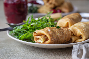 Homemade stuffed thin pancakes or crepes with meat, spicy cranberry sauce and arugula, light stone background. Traditional Russian cuisine for Maslenitsa. Shrove Tuesday.