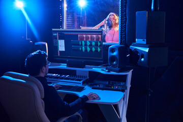 Professional male sound engineer mixing audio in recording studio. Music production technology, girl singing into microphone