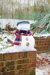 A snowman in a protective mask welcomes the first snow in London in 2021. Winter day during the pandemic coronavirus.