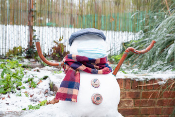 A snowman in a protective mask welcomes the first snow in London in 2021. Winter day during the pandemic coronavirus.