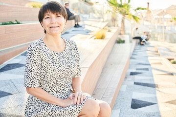 Portrait of 50 year old happy caucasian woman sitting and smiling in the park on the bench, adult...