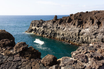 Fototapeta na wymiar Volcanic coastline by the sea in Los Hervideros tourist attraction in Lanzarote island. Blue ocean water splashing over black rocks cliffs
