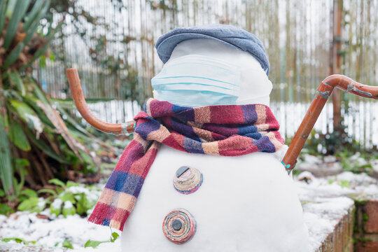 A snowman in a protective mask welcomes the first snow in London in 2021. Winter day during the pandemic coronavirus.