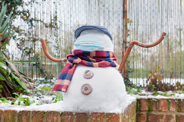 A snowman in a protective mask welcomes the first snow in London in 2021. Winter day during the pandemic coronavirus.