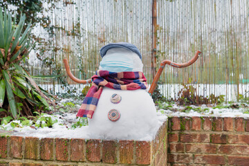 A snowman in a protective mask welcomes the first snow in London in 2021. Winter day during the pandemic coronavirus.