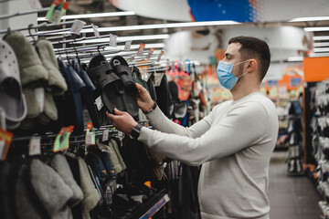 Young man wearing medical mask chooses home slippers in supermarket mall