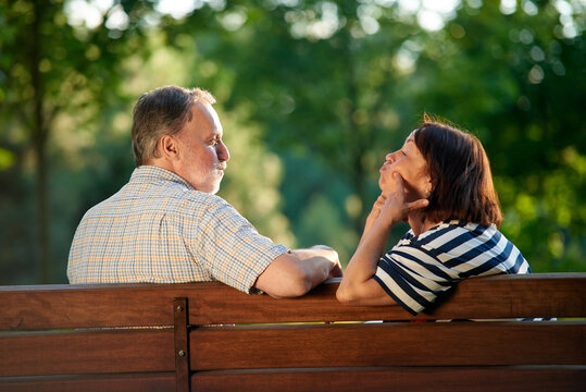 Back view retired couple fooling around on the bench. Man and woman making funny faces.