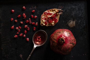 Ripe pomegranate with juicy fresh seeds in a spoon. Top view on a dark metal table