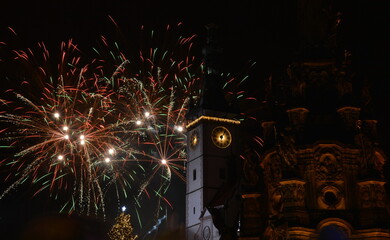 Green and red fireworks exploding behind a clock tower and Holy Trinity Column in Olomouc, Czech...