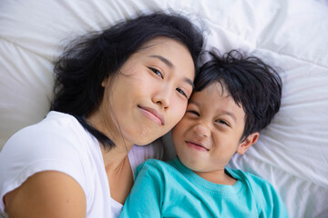 Authentic close up of happy mother and her son in a bed. Concept of new generation, family, parenthood, authenticity, connection.