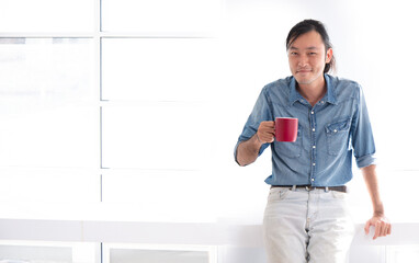 Obraz premium asian guy smile with red cup of hot coffee in the morning