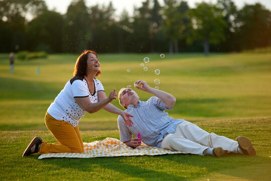 Happy married couple blowing bubbles. Retired couple having fun on the green field.