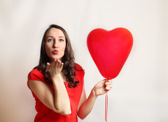 Beautiful woman sends air kiss with red balloon heart shape over white background. Beautiful happy young woman on a birthday holiday, Valentine's day, Mothers day. Close-up