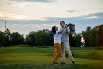 Obraz premium Happy couple dancing outdoors. Mature man and woman on the green field.