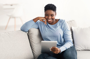 Black woman sitting on couch and using tablet