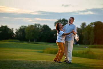 Obraz premium Mature couple dancing tango outdoors. Man and woman on the green field.