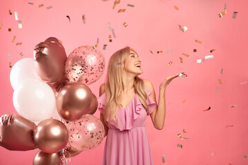 Charming young lady holding balloons, having birthday party over pink background with falling...