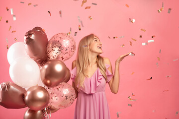 Obraz na płótnie Canvas Charming young lady holding balloons, having birthday party over pink background with falling confetti, free space
