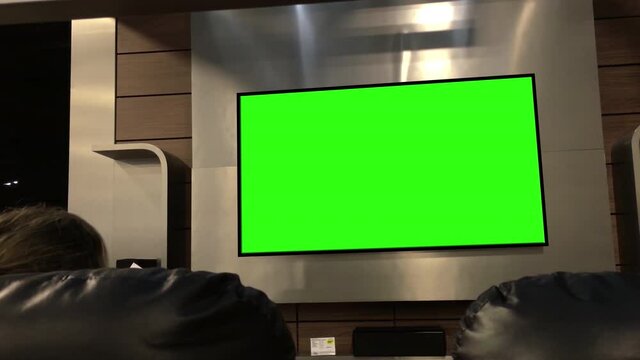 A customer sitting on the sofa watching display tv with a green screen inside the electrical store with 4k resolution
