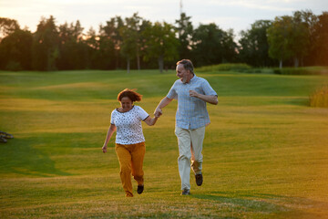 Naklejka na ściany i meble Happy laughing couple running on the grass. Man and woman holding hands. Green field background.