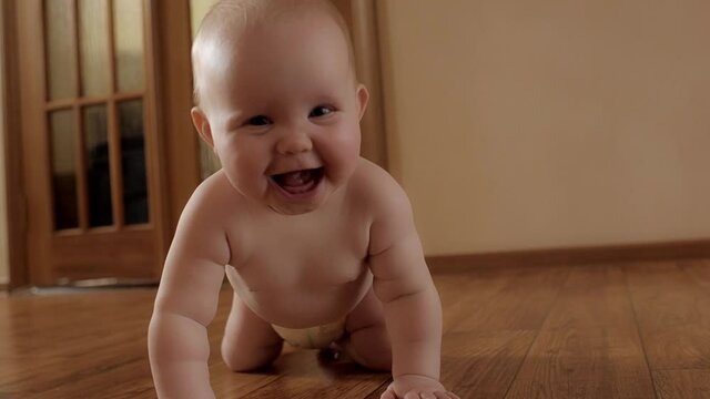 Cute little baby in diaper laughing rejoicing crawling on wooden floor at home joyful child smiling