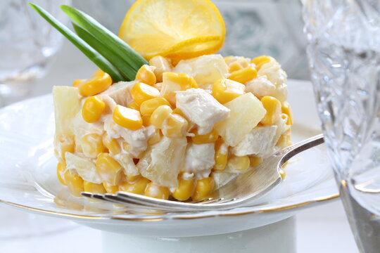 Salad with chicken, pineapple and corn with champagne on a white plate