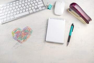 Colored paper clips in the form of a heart on a desktop with a blank notepad for writing. Valentine's Day in the office. Top view