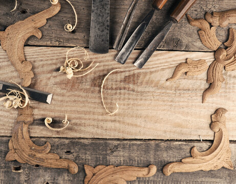 Carved oak decorative elements on a rustic workbench with chisels, wood working concept