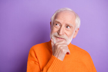 Portrait of aged man arm on chin look empty space thinking wear pullover isolated on purple color...